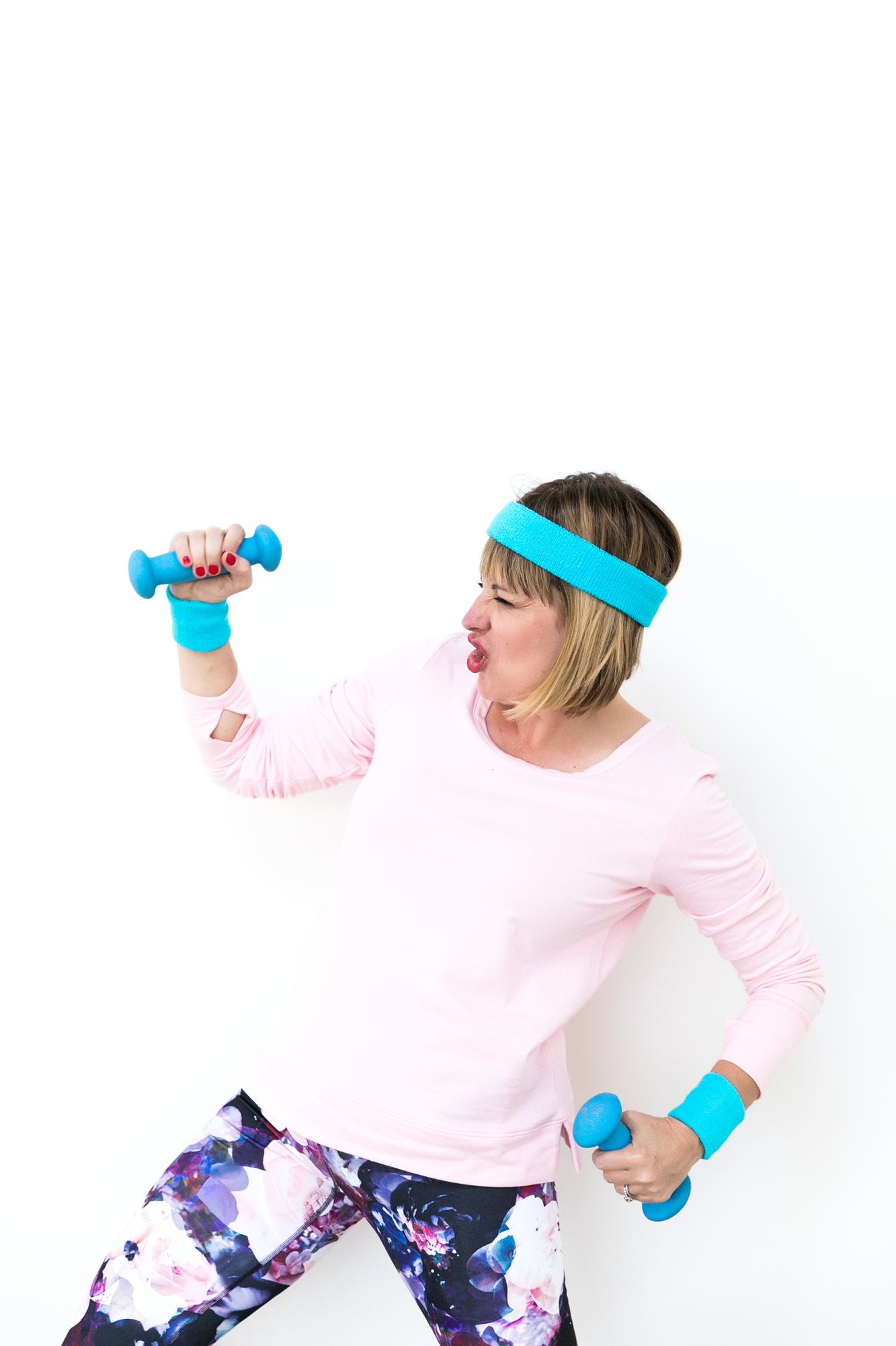 Kara in a pink sweatshirt and blue sweatband curling little blue dumbbells