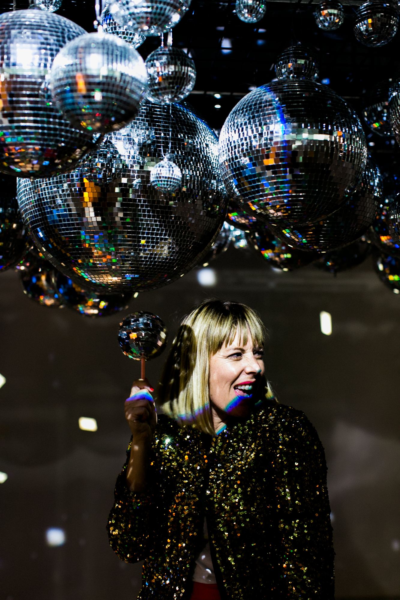 Kara under a ceiling of disco balls in a sequin jacket