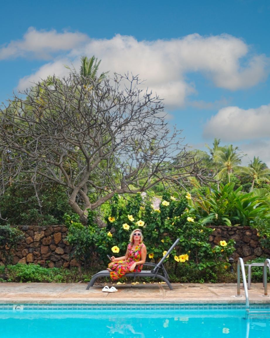 Kara alone on a poolside lounger under a big tree